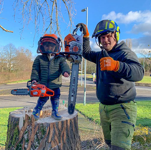 Hywel Jones, qualified tree surgeon, holding a chainsaw beside a young apprentice on a freshly cut stump in Pontypool