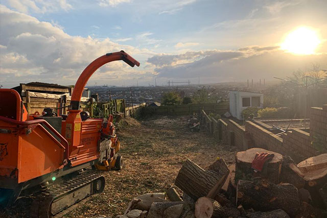 Wood chipper processing branches at sunset above the South Wales valleys